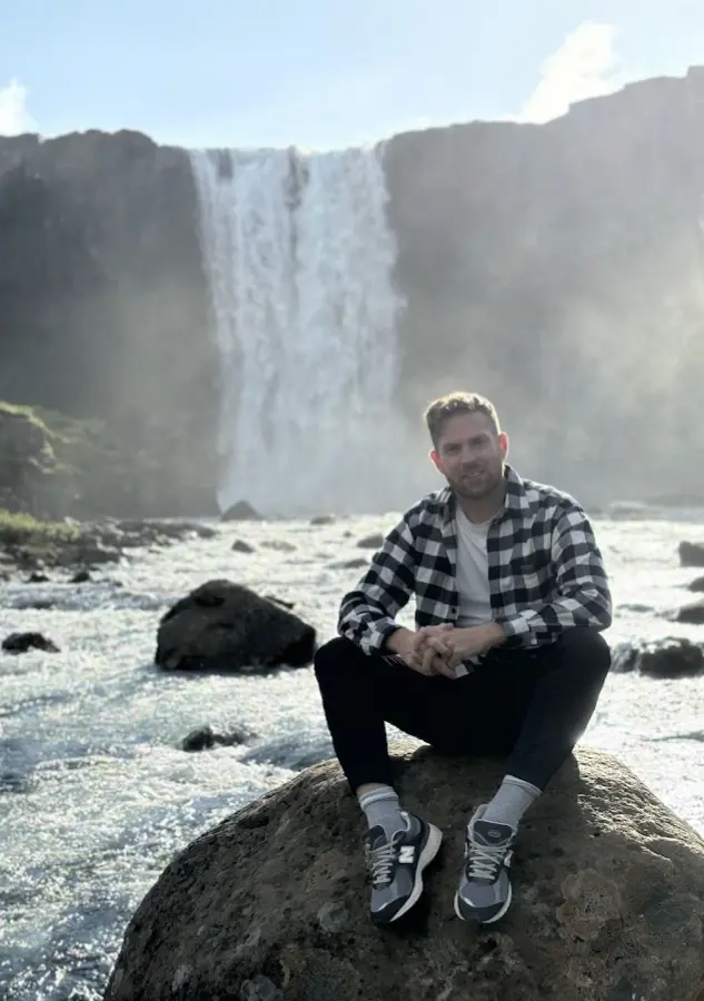 Benjamin Snorrason sitting in front of a waterfall in Iceland
